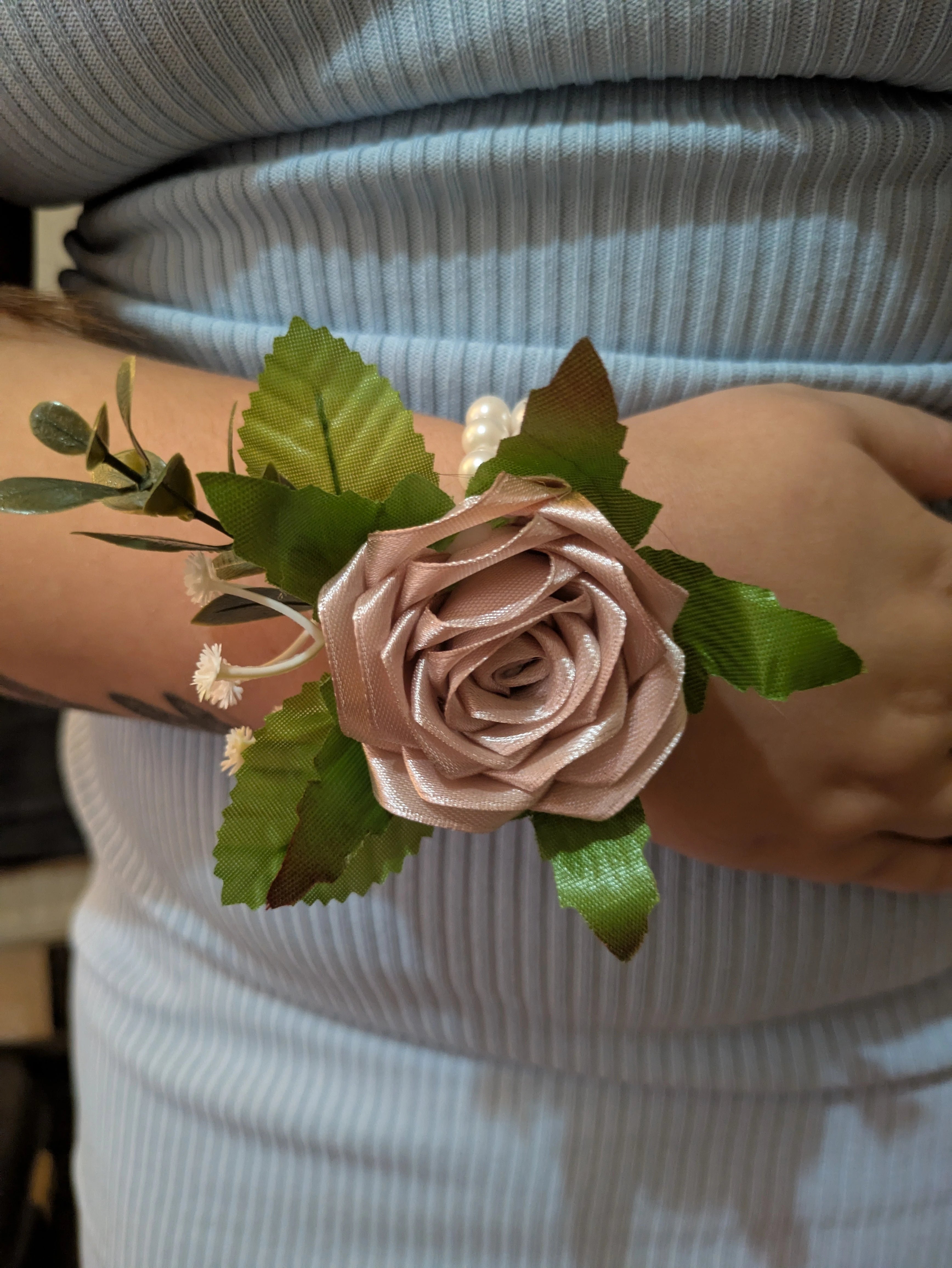 Wrist corsage with satin roses and green leaves worn on wrist for weddings and prom