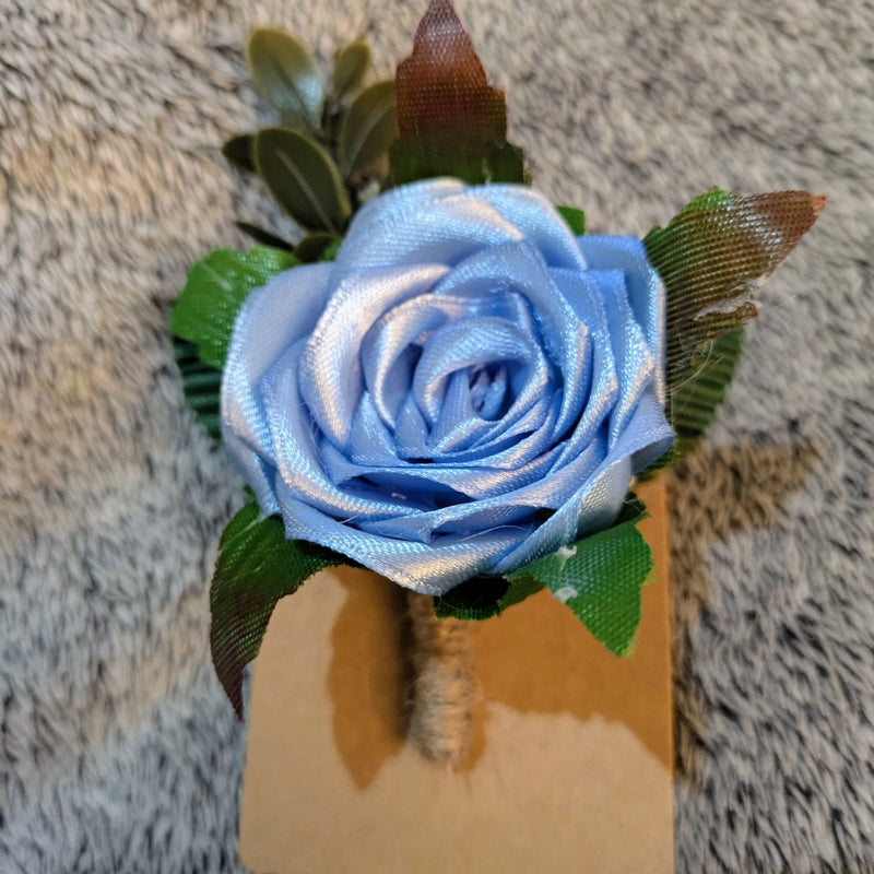 Blue satin rose boutonniere for weddings and proms with green leaves on a textured background