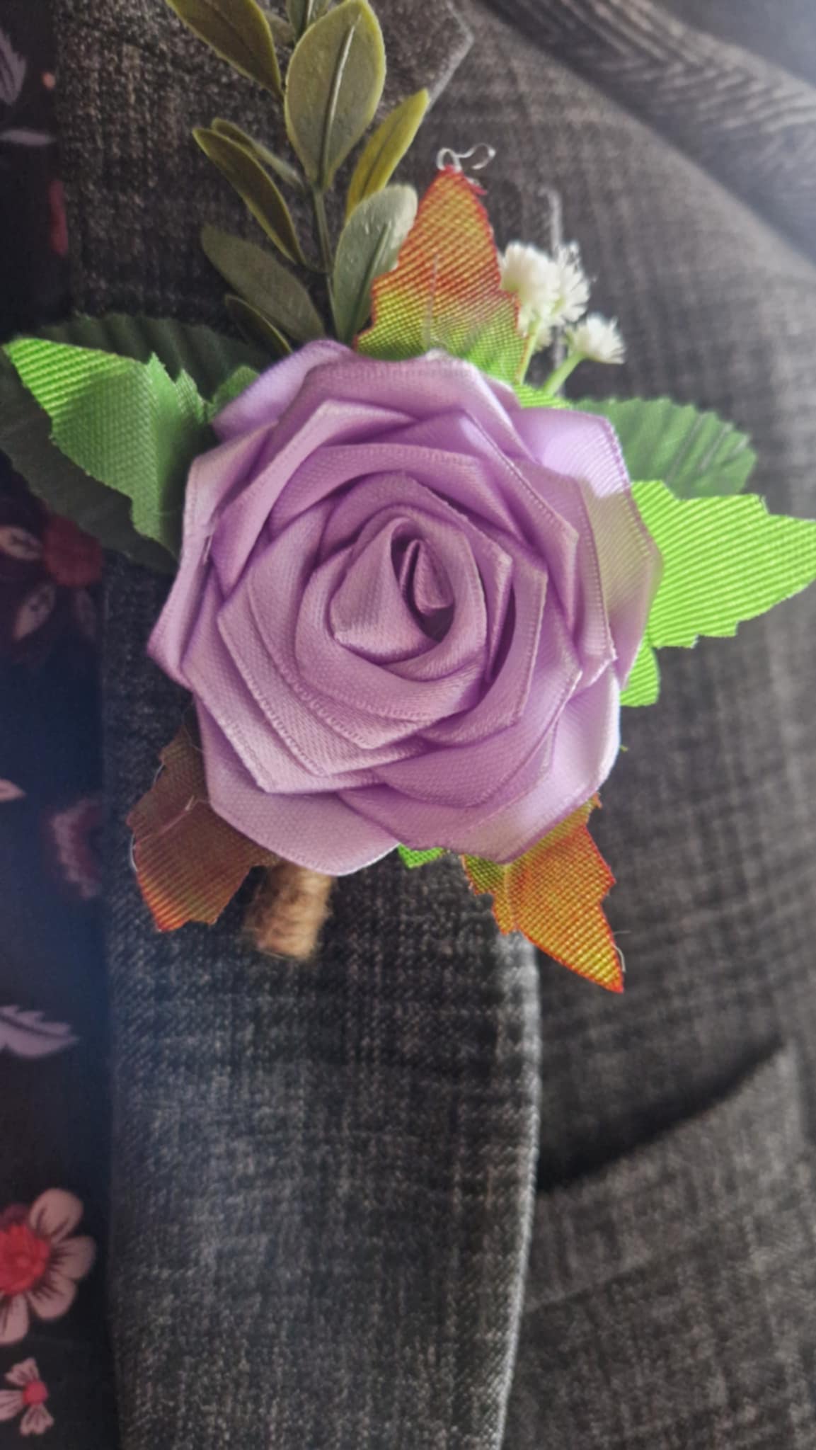 Handmade light orchid satin rose boutonniere pinned on dark gray suit lapel with green leaves