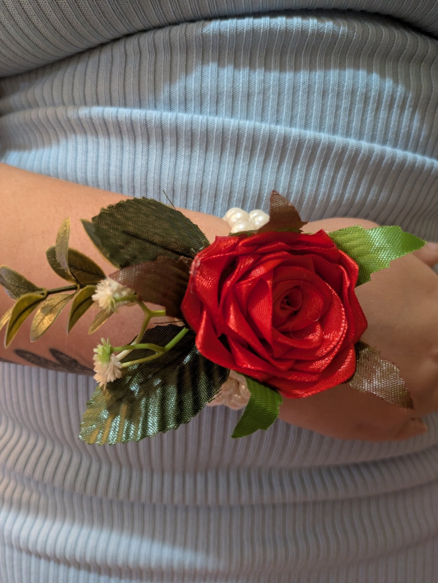 Handmade Red Satin Rose Corsages with green leaves and white pearls worn on wrist over ribbed gray fabric